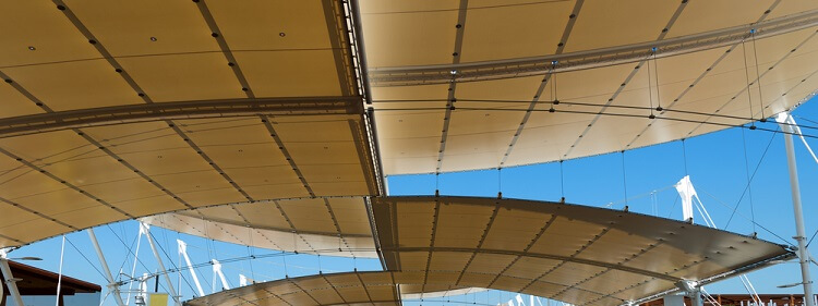 Detail of a modern tensile structure, membrane fabric roof with poles and steel cables, on a blue clear sky